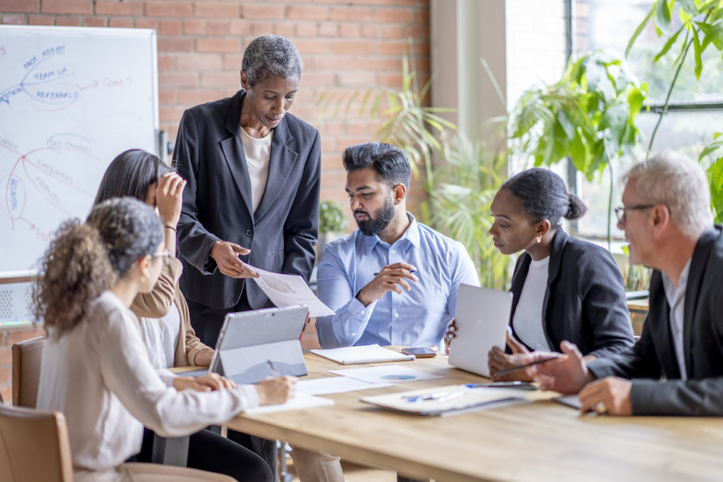 A small group of mature corporate business people, gather around a boardroom table as they meet to discuss the company.