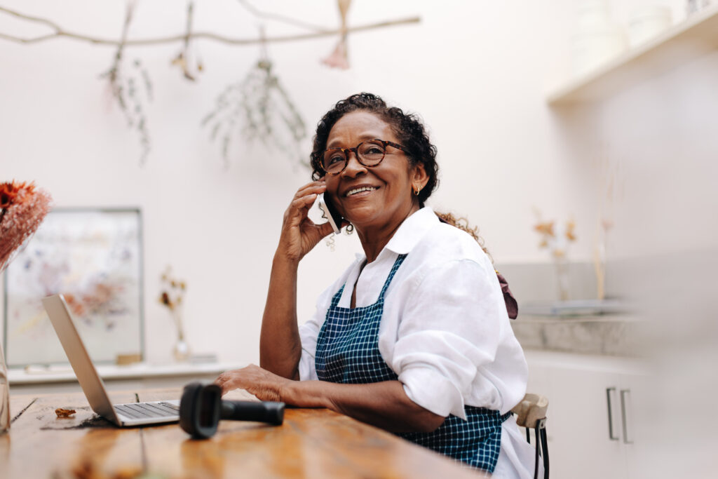 Happy flower store owner talks with her clients on a phone call, using her communication skills to build strong relationships with her customers.